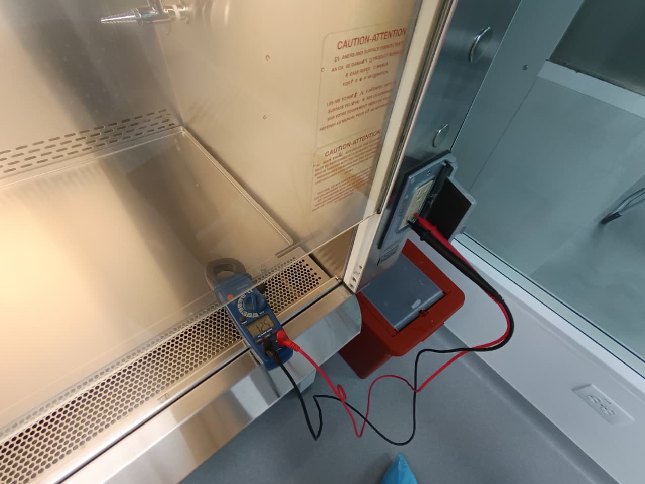 Diagnóstico eléctrico con multímetro en gabinete de acero inoxidable de equipo biomédico durante mantenimiento preventivo